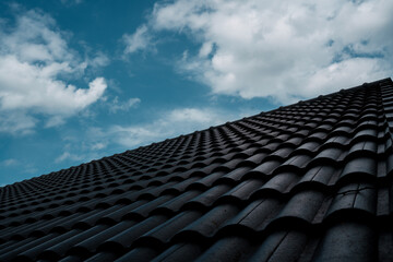 Fototapeta premium A close-up of a house roof lined with grey tiles, showing the architectural design, roofing materials and construction details under a bright blue sky.