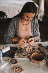 Portrait of a young brunette woman jewelry designer. She is sitting at a work table on which lie tools and various beads from which she creates jewelry. Home small business, startup. Creative hobby.