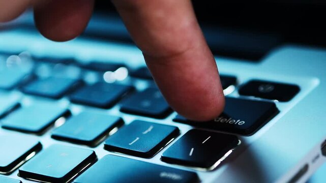 Finger of the computer user, he presses the delete button on the computer keyboard.
