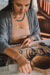 Portrait of a young brunette woman jewelry designer. She is sitting at a work table on which lie tools and various beads from which she creates jewelry. Home small business, startup. Creative hobby.