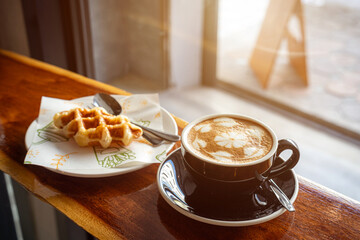 Hot coffee latte with latte art milk foam in cup mug and Homemade Belgian Waffles with honey on wood desk on top view. As breakfast In a coffee shop at the cafe,during business work.