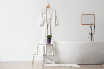 Pot with lavender flowers and towel on coffee table near bathtub in modern bathroom