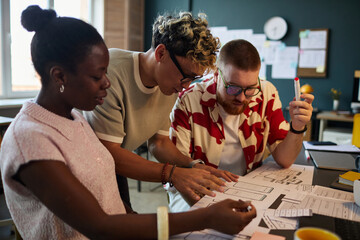 Multiethnic group of young adults collaborating on project, discussing design sketches and...