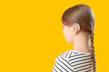 Little girl with hearing aid on yellow background