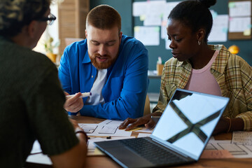 Caucasian young adult man and Black young adult woman collaborating with another at table,...