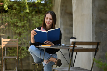 Relaxed Caucasian adult student enjoying reading in a peaceful outdoor setting, surrounded by greenery