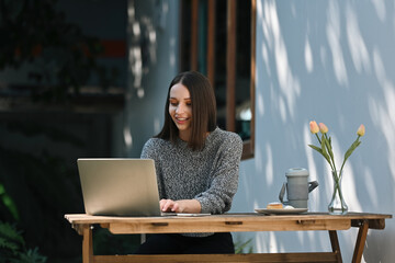 A White Female freelancer typing on her laptop in a garden workspace