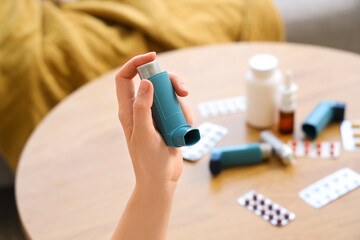Woman holding modern inhaler over table with different medicine in living room, closeup