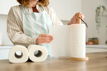 Young woman with rolls of paper towels near table in kitchen, closeup