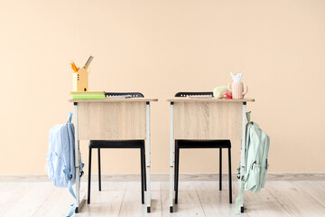 Modern school desks with backpacks, books and stationery on beige background