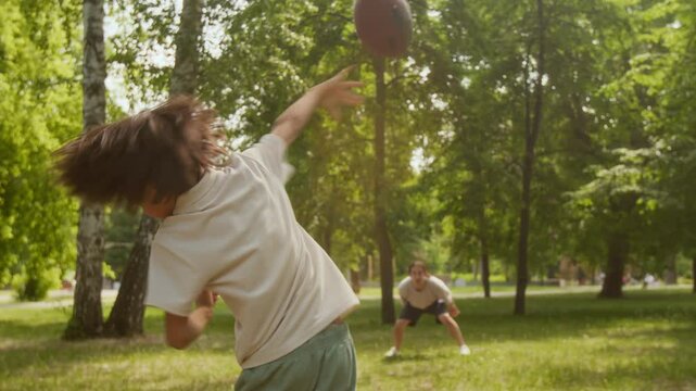 Young boy playing American football ball with his father in park, spending family time together on sunny weekend day