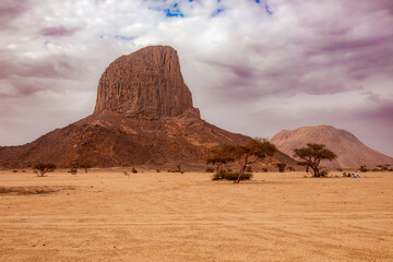 A wide, low-angle shot captures a vast desert plain leading towards a striking, isolated rock...