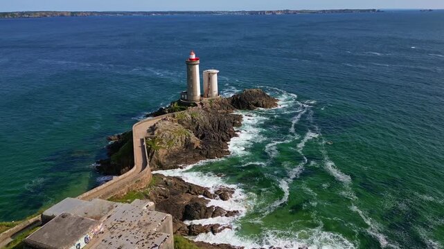 Drone in downward motion follows the stone path to Petit Minou lighthouse. Waves crash around the rocks and the sea stretches to the horizon - Brittany, France
