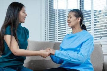 An Asian mother and daughter sit closely on a sofa, sharing a warm embrace. Their gentle...