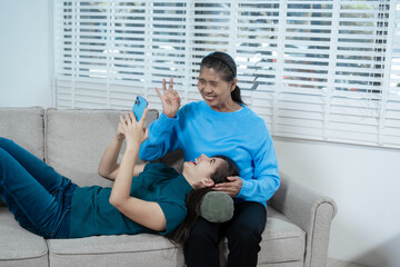 An Asian mother and daughter sit closely on a sofa, sharing a warm embrace. Their gentle...