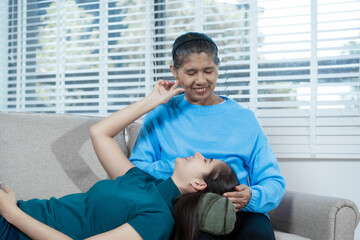 An Asian mother and daughter sit closely on a sofa, sharing a warm embrace. Their gentle...