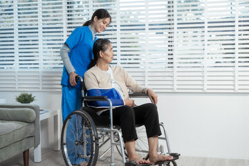 A young Asian nurse attentively takes notes while conversing with an elderly woman in a wheelchair...