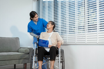 A young Asian nurse attentively takes notes while conversing with an elderly woman in a wheelchair...