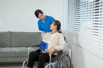 A young Asian nurse attentively takes notes while conversing with an elderly woman in a wheelchair...