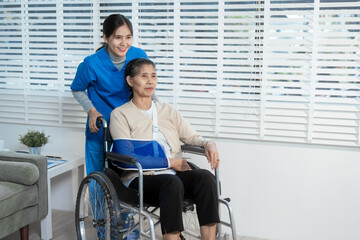 A young Asian nurse attentively takes notes while conversing with an elderly woman in a wheelchair...