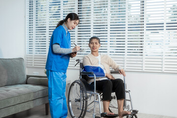 A young Asian nurse attentively takes notes while conversing with an elderly woman in a wheelchair...
