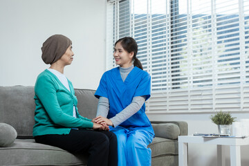 A young Asian nurse gently holds hands with a patient wearing a headscarf,possibly indicating...