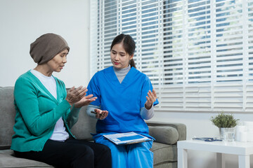 A young Asian nurse gently holds hands with a patient wearing a headscarf,possibly indicating...
