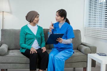 A young Asian nurse gently holds hands with a patient wearing a headscarf,possibly indicating...