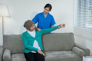 A young Asian nurse gently holds hands with a patient wearing a headscarf,possibly indicating...
