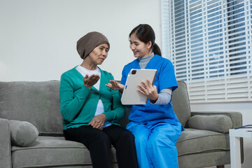 A young Asian nurse gently holds hands with a patient wearing a headscarf,possibly indicating...