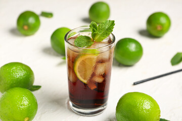 Glass of cold Cuba Libre cocktail with mint and limes on white background, closeup