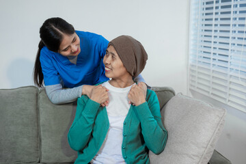 A young Asian nurse gently holds hands with a patient wearing a headscarf,possibly indicating...