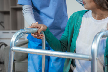 A young Asian nurse assists an elderly female cancer patient, wearing a headscarf, with using a...