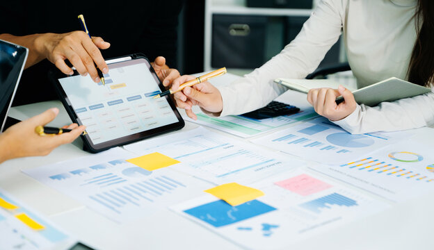 Business documents on office table with smart phone and calculator digital tablet and graph business with social network diagram and two colleagues discussing data working in the office