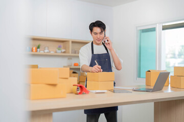 E-commerce. Young man on phone while managing packages and writing notes in a modern workspace.