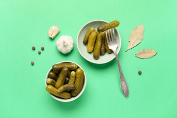 Bowls with tasty pickled cucumbers and different spices on green background