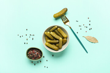 Bowl with tasty pickled cucumbers, peppercorns and bay leaf on turquoise background