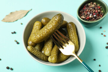 Bowl with tasty pickled cucumbers, peppercorns and bay leaf on turquoise background, closeup