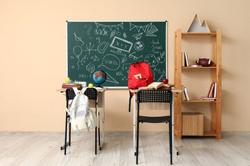 Interior of empty classroom with school desks, shelving unit and chalkboard