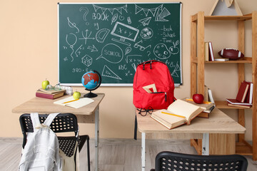 Interior of empty classroom with school desks, shelving unit and chalkboard
