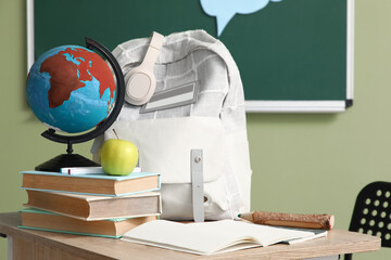 School desk with backpack, apple, books and globe in classroom
