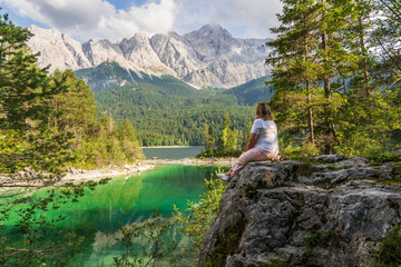 Traveler woman admiring crystal clear Eibsee lake and Bavarian Alps from rocky viewpoint. Peaceful...