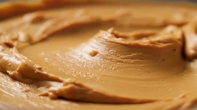 Close-up of thick, creamy peanut butter with crunchy bits, rotating to reveal swirl patterns, rich texture, and natural gloss in smooth motion.

