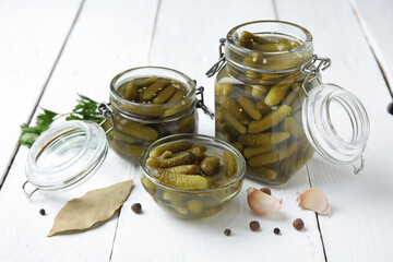 Jars with tasty pickled cucumbers and different spices on white wooden background