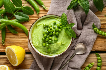 Bowl of mashed green peas with mint and lemon on wooden background