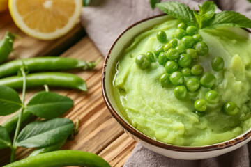 Bowl of mashed green peas with mint and lemon on wooden background, closeup
