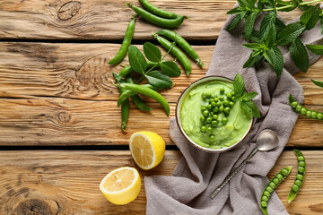 Bowl of mashed green peas with mint and lemon on wooden background