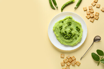 Plate with mashed green peas and crackers on yellow background
