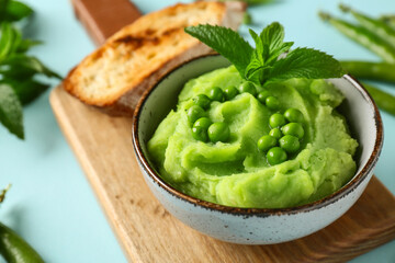 Bowl of mashed green peas with mint and bread slice on blue background, closeup