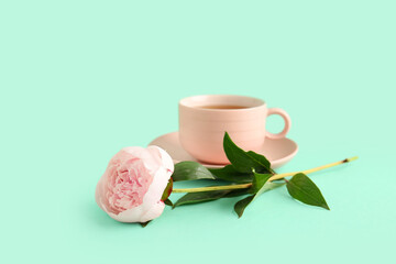Beautiful peony flower and cup of hot tea on turquoise background